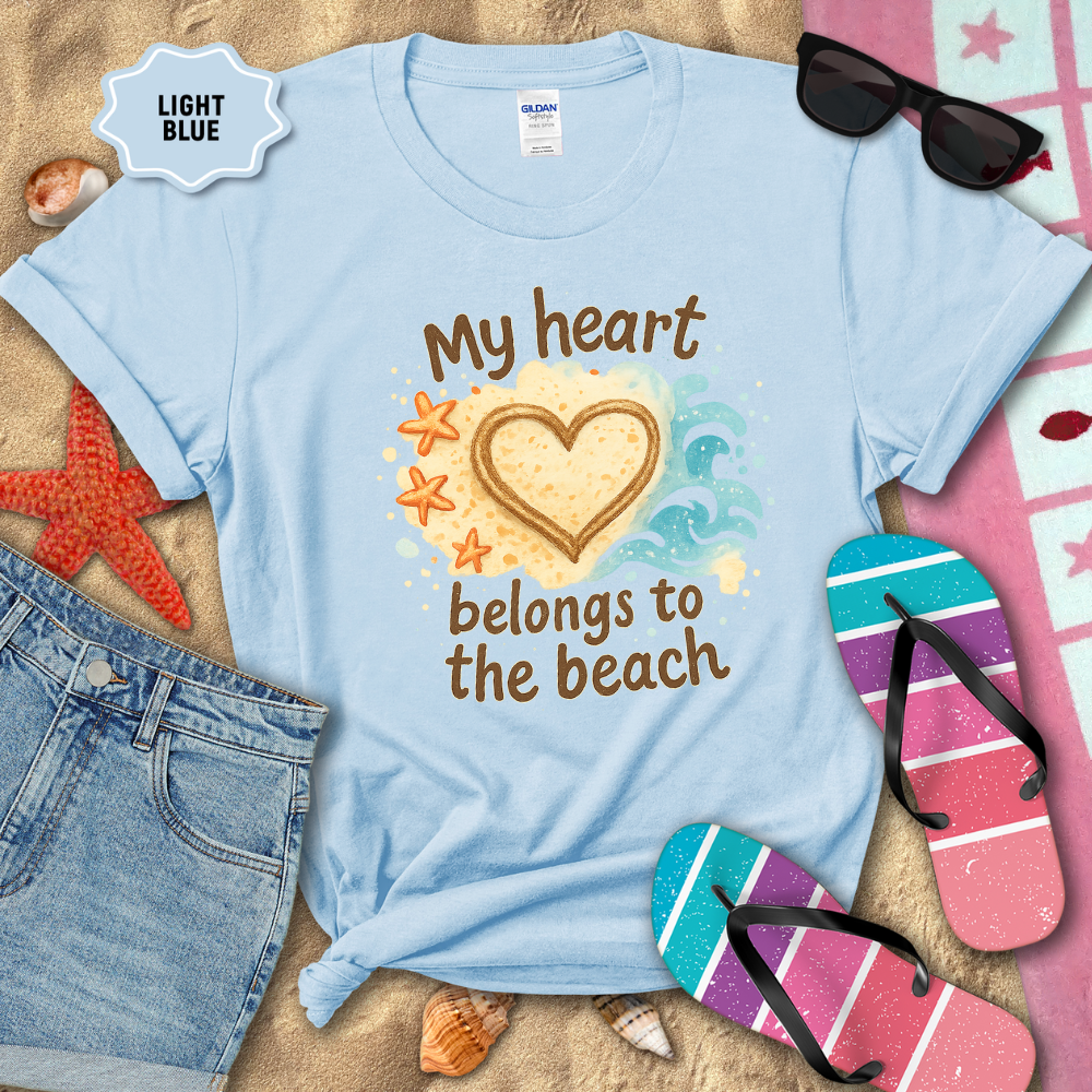 Light blue t-shirt with 'My heart belongs to the beach' design on sand with beach accessories.