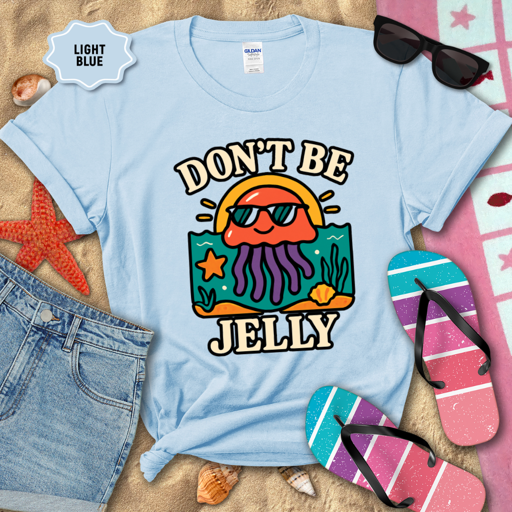 Light blue t-shirt with 'Don't Be Jelly' design on sand with beach accessories.