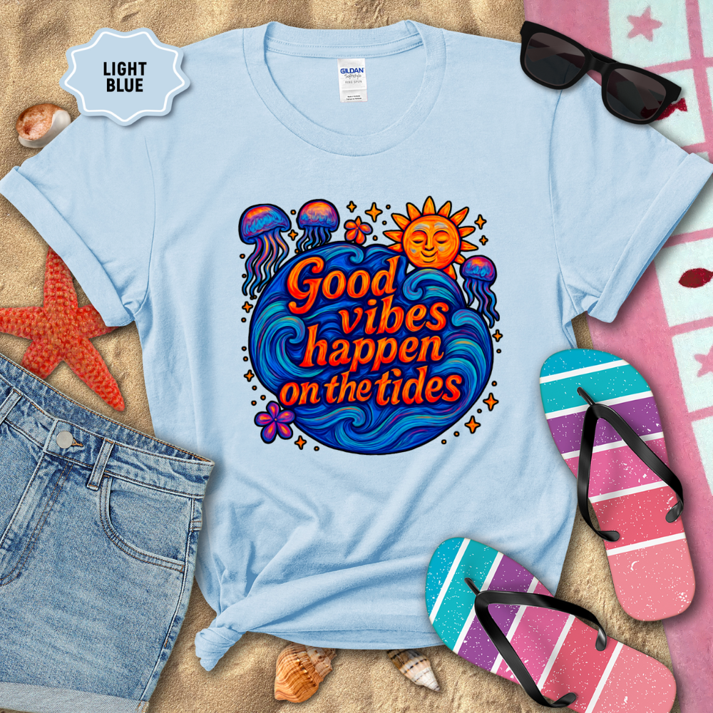 Light blue t-shirt with 'Good vibes happen on the tides' design, surrounded by beach accessories.