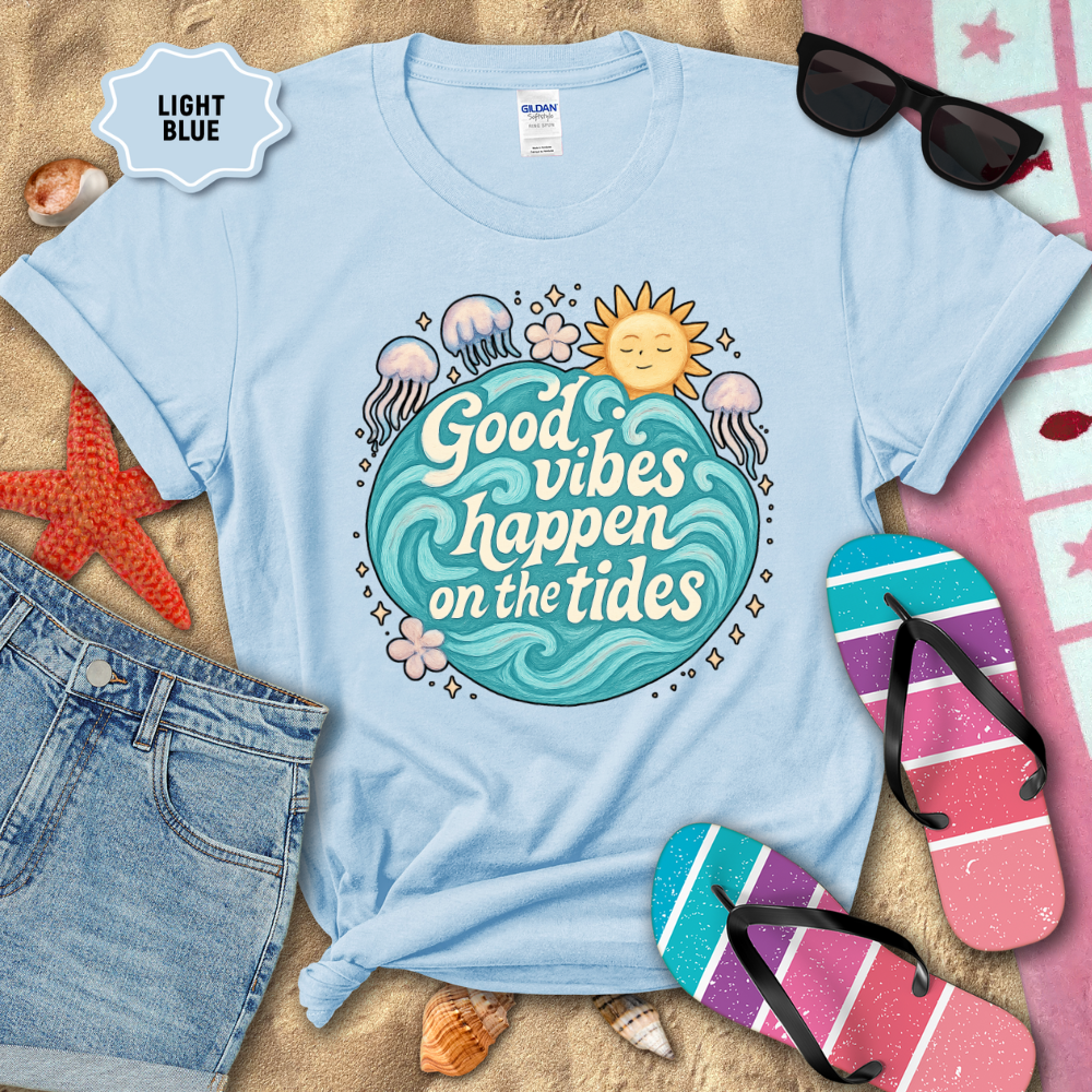 Light blue t-shirt with 'Good vibes happen on the tides' design, surrounded by beach accessories.