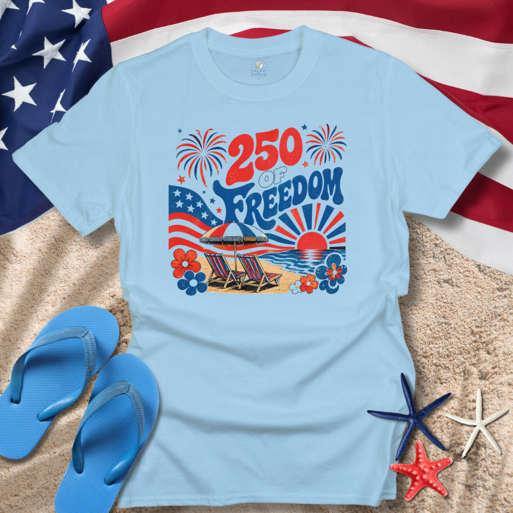 Light blue t-shirt with beach-themed design featuring '250 of Freedom' text, American flag, and beach elements on sand with flip-flops and starfish.