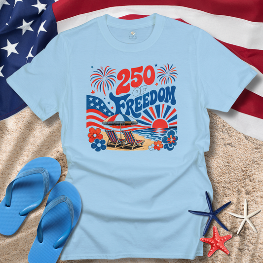 Light blue t-shirt with beach-themed design featuring '250 of Freedom' text, American flag, and beach elements on sand with flip-flops and starfish.