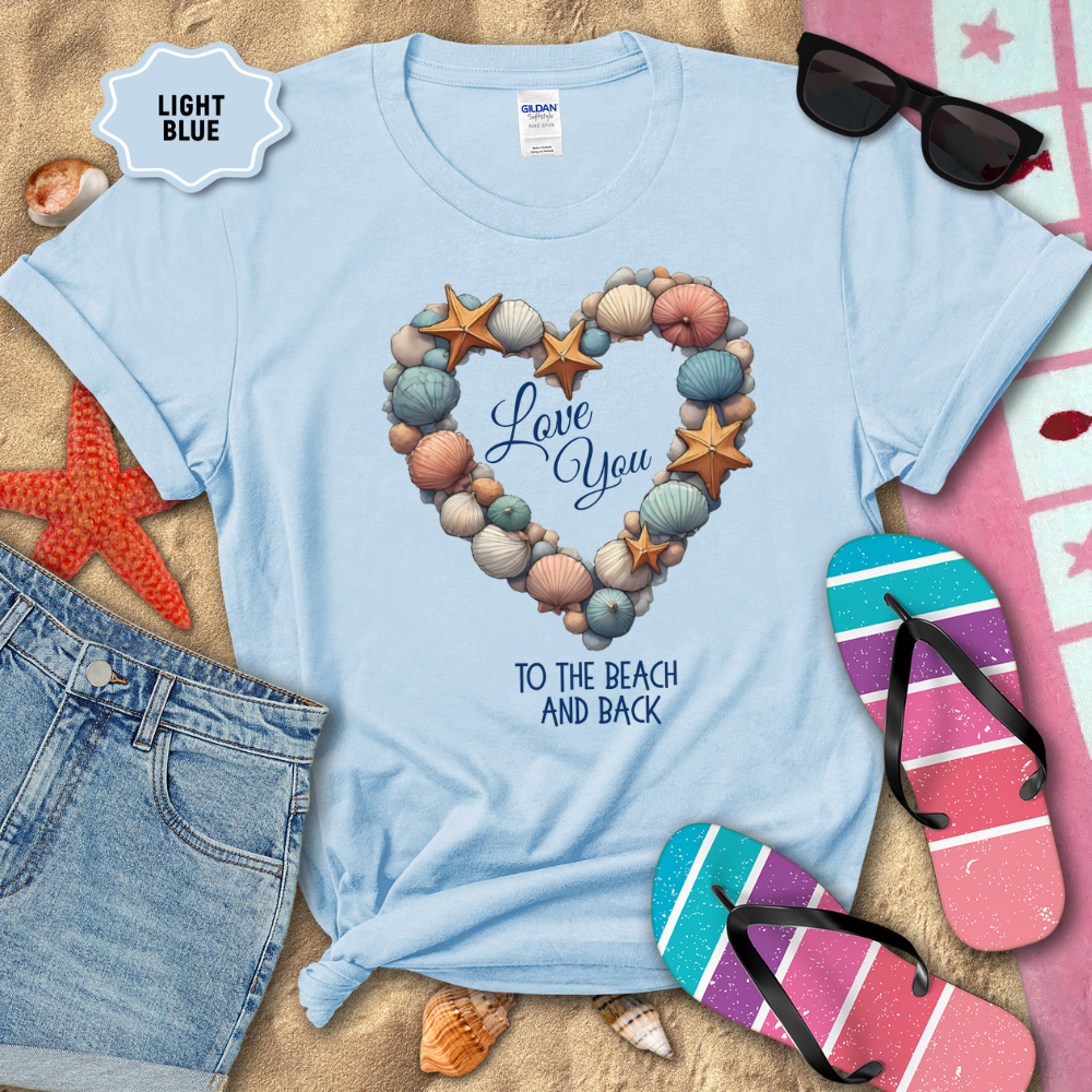 Light blue t-shirt with beach-themed design on sand with sunglasses, flip-flops, and denim shorts.