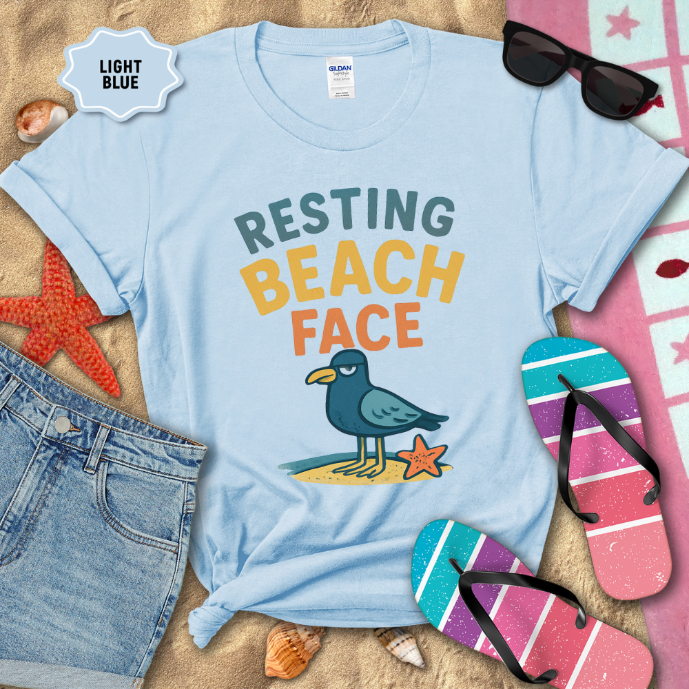 Light blue t-shirt with 'Resting Beach Face' graphic on sand with beach accessories.