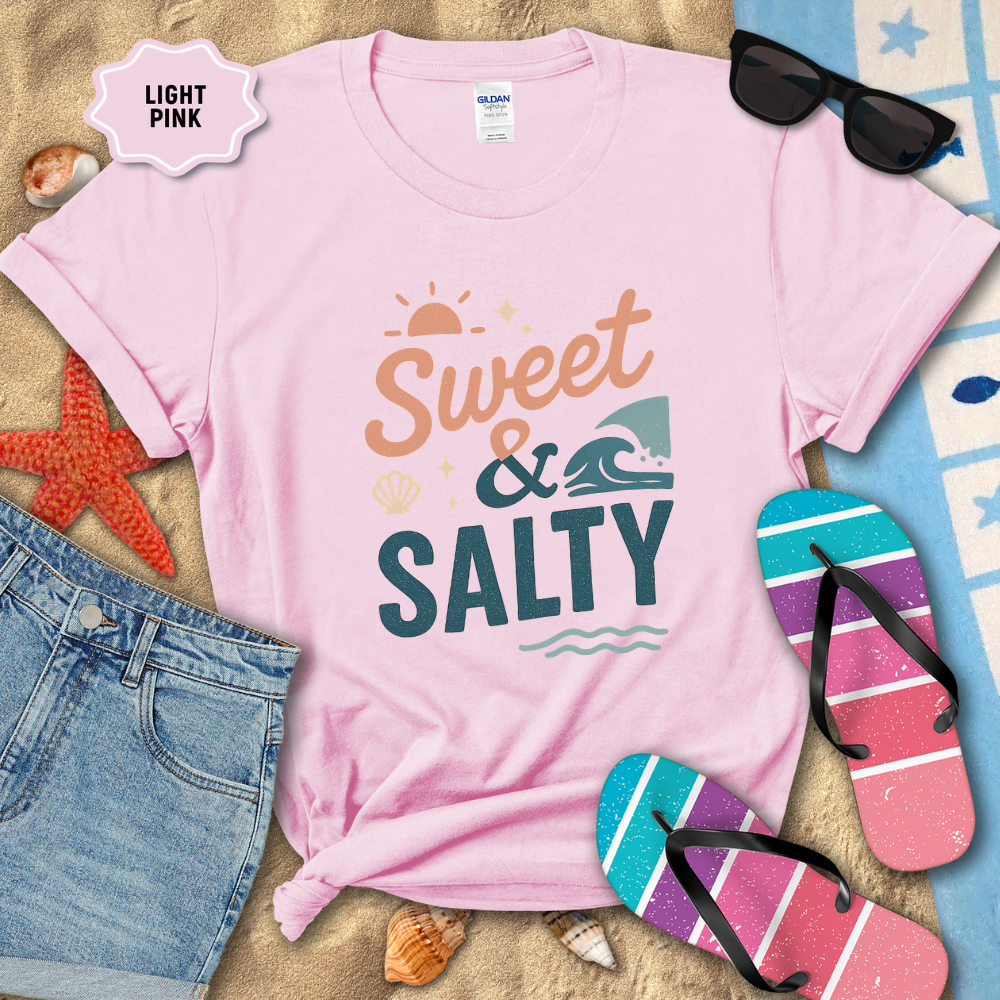 Light pink t-shirt with 'Sweet & Salty' text, sunglasses, and flip-flops on a sandy background