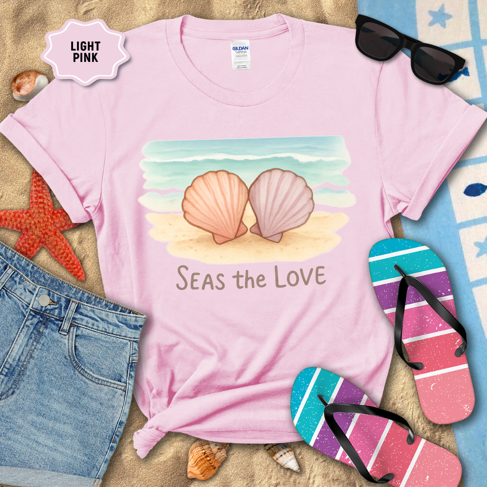 Light pink t-shirt with shell design and 'Seas the Love' text, surrounded by beach accessories.