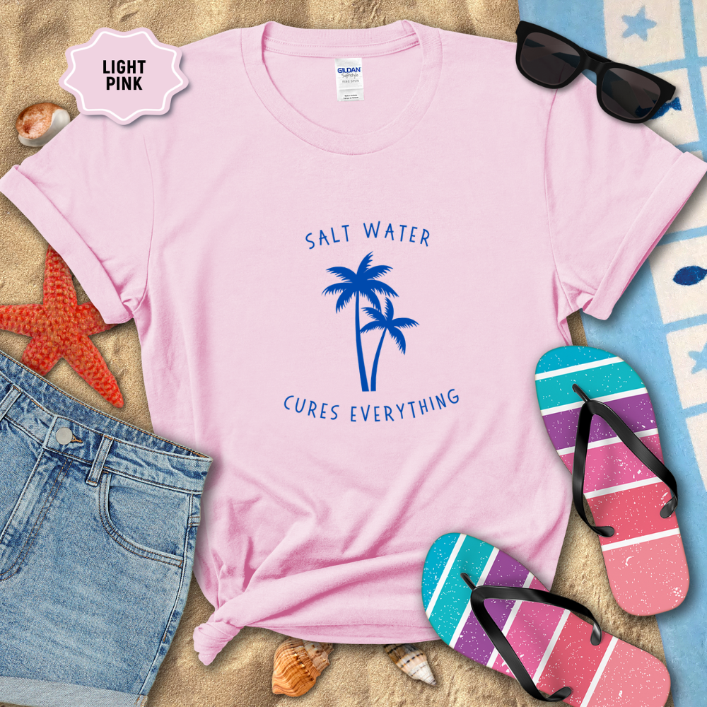 Light pink t-shirt with 'Salt Water Cures Everything' design, sunglasses, flip-flops, and beach items on sand.