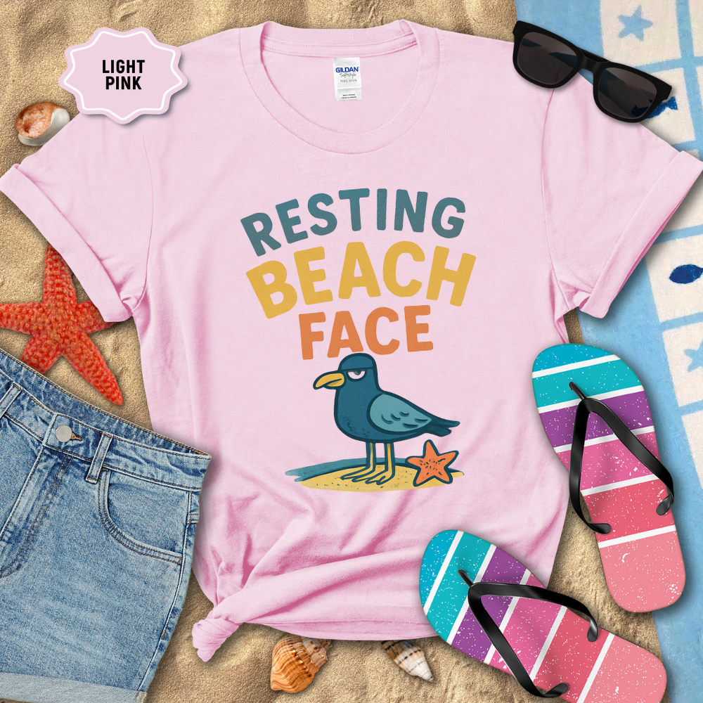 Light pink t-shirt with 'Resting Beach Face' design, sunglasses, and flip-flops on a sandy background