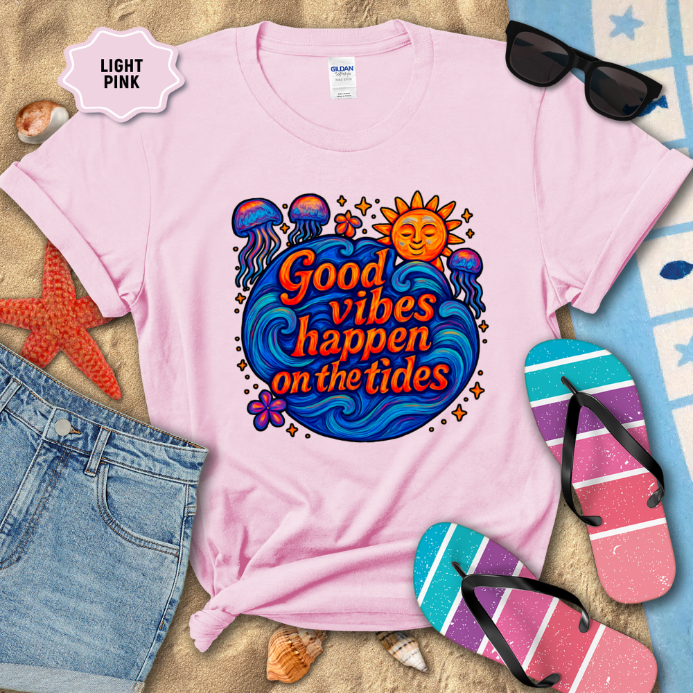 Light pink t-shirt with 'Good vibes happen on the tides' design, surrounded by beach accessories.