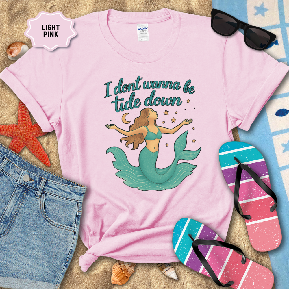 Light pink t-shirt with mermaid graphic and text on a beach-themed background