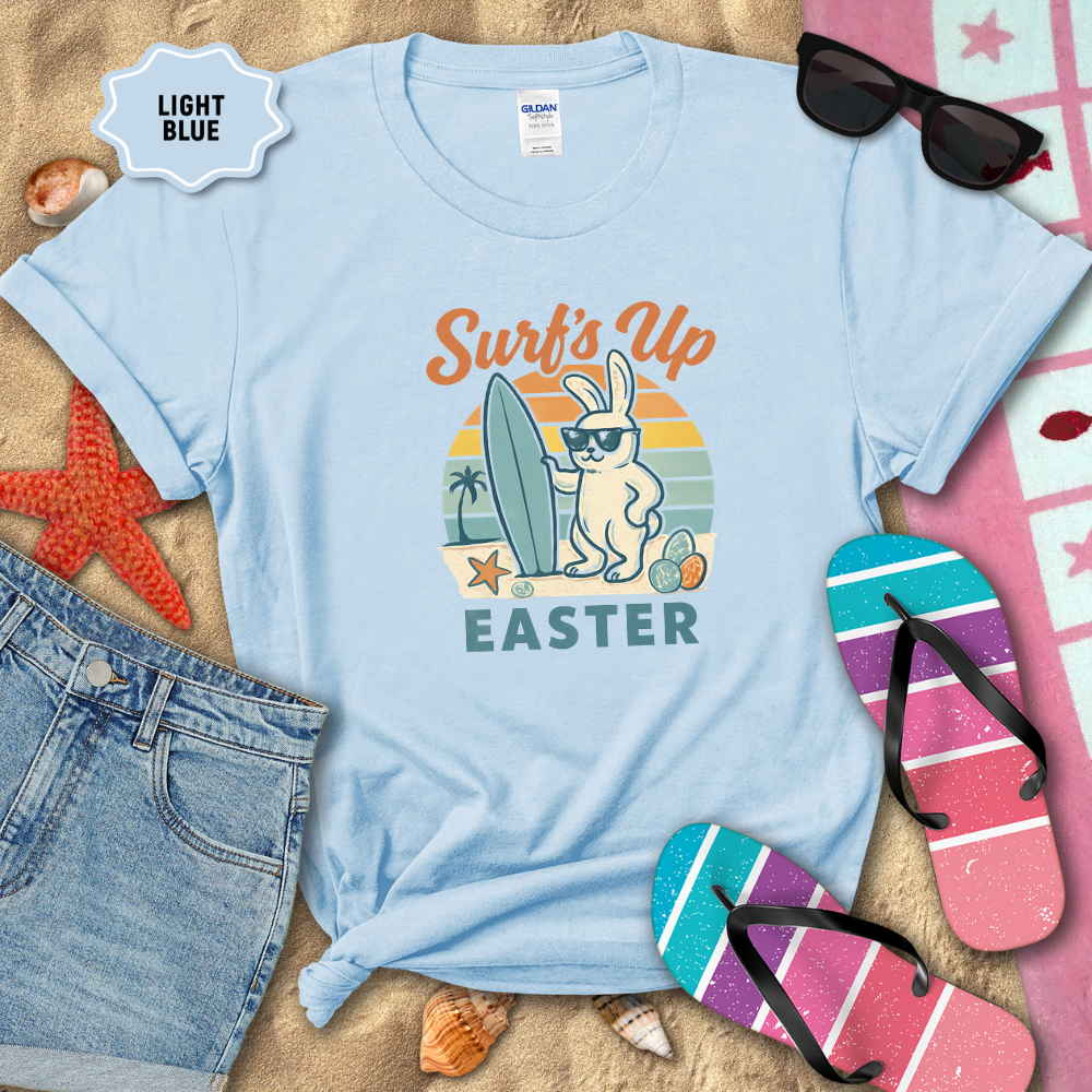 Light blue t-shirt with Easter bunny graphic on sand with beach accessories