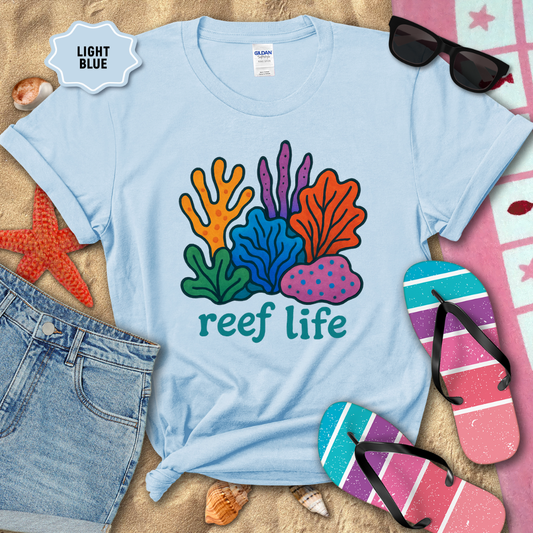 Light blue t-shirt with 'reef life' design surrounded by beach items on sand