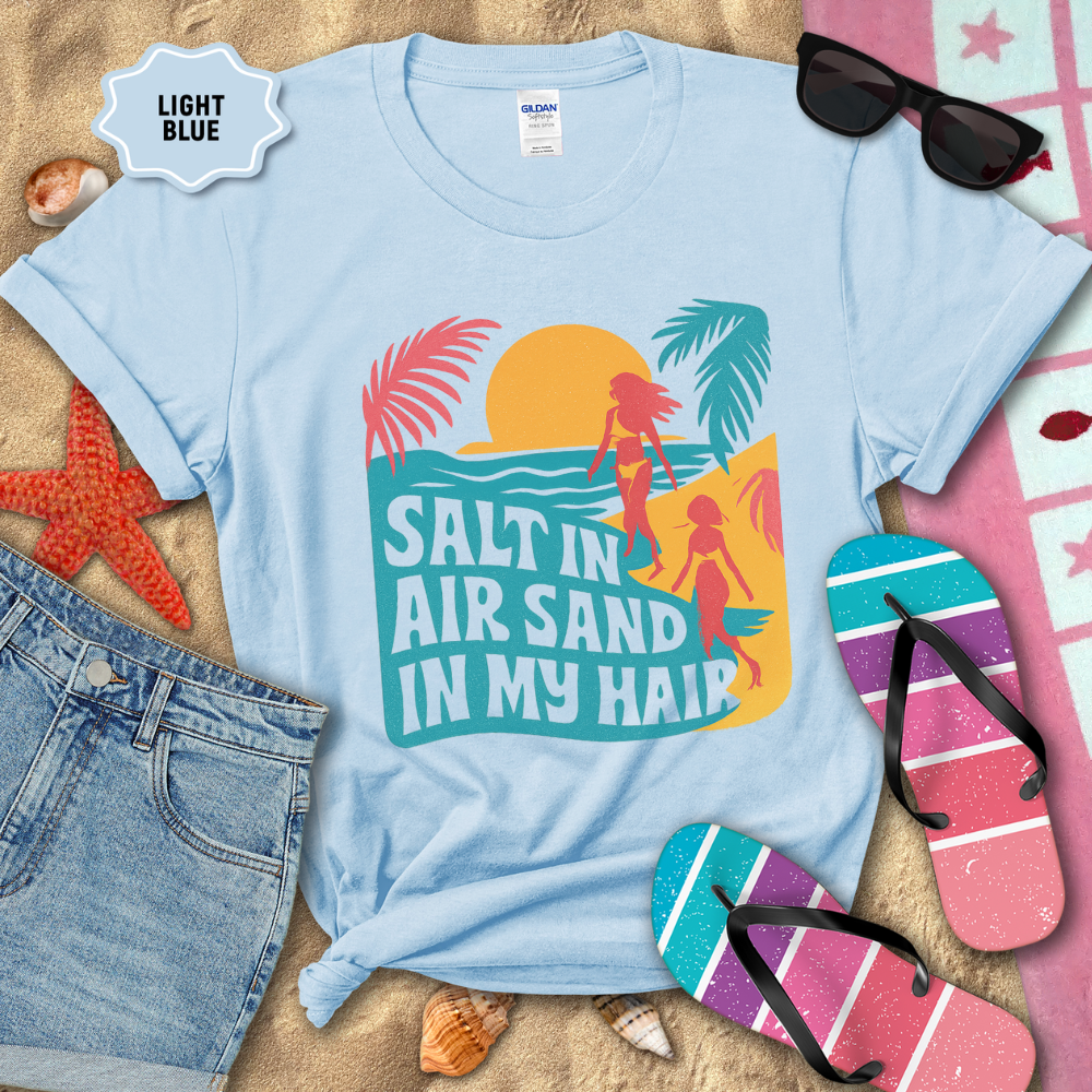 Light blue t-shirt with beach-themed design and accessories on sand