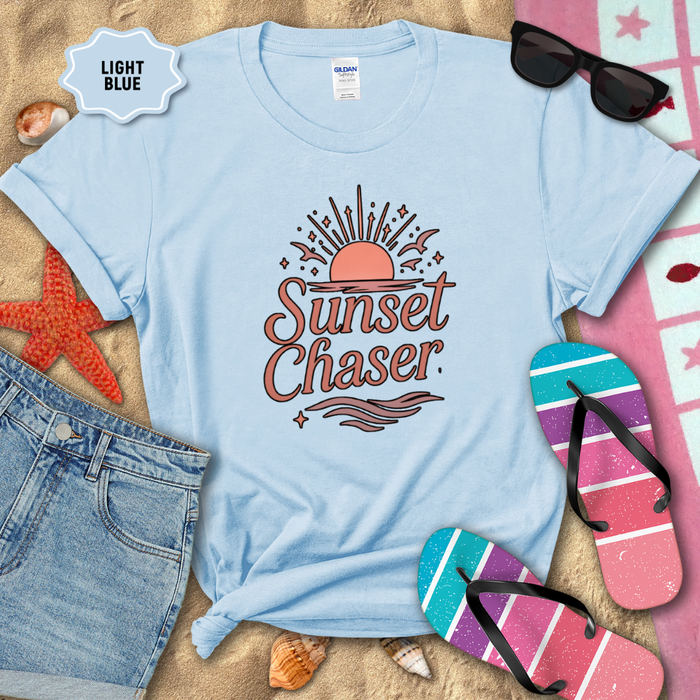 Light blue t-shirt with 'Sunset Chaser' design on a sandy background with beach accessories.