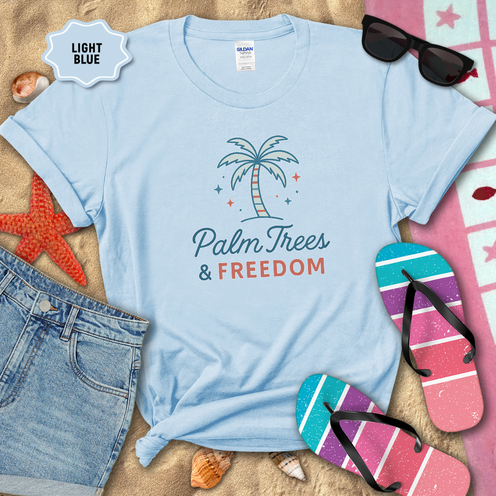 Light blue t-shirt with 'Palm Trees & Freedom' design on a sandy background with beach accessories.