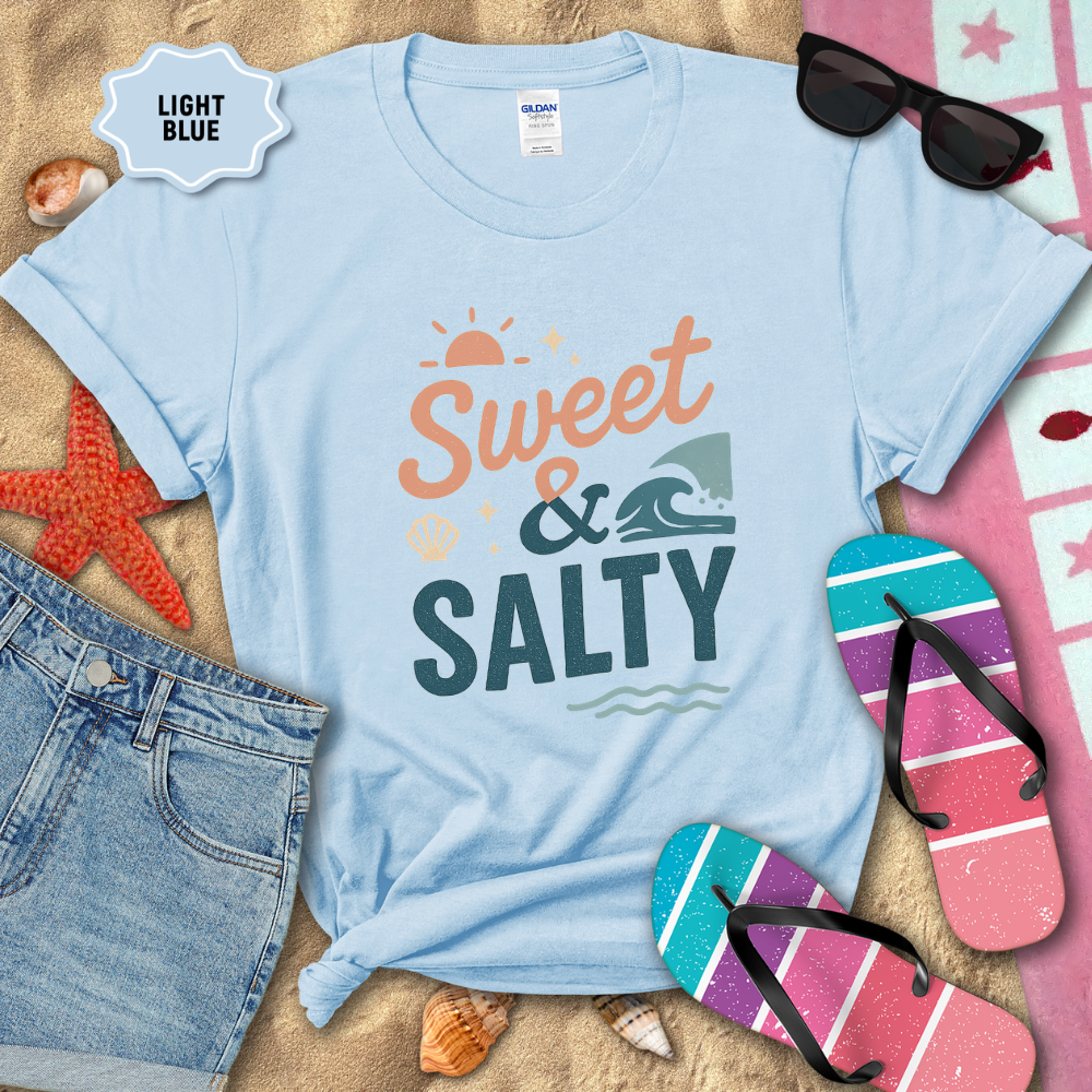 Light blue t-shirt with 'Sweet & Salty' text on a sandy background with beach accessories.