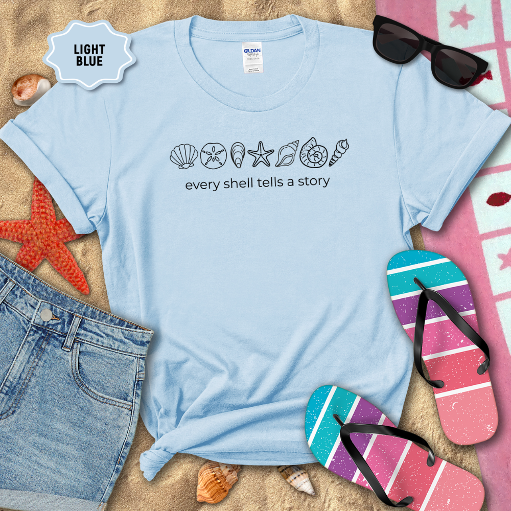 Light blue t-shirt with fish illustrations and 'Unity in Diversity' text on a sandy background with beach accessories.