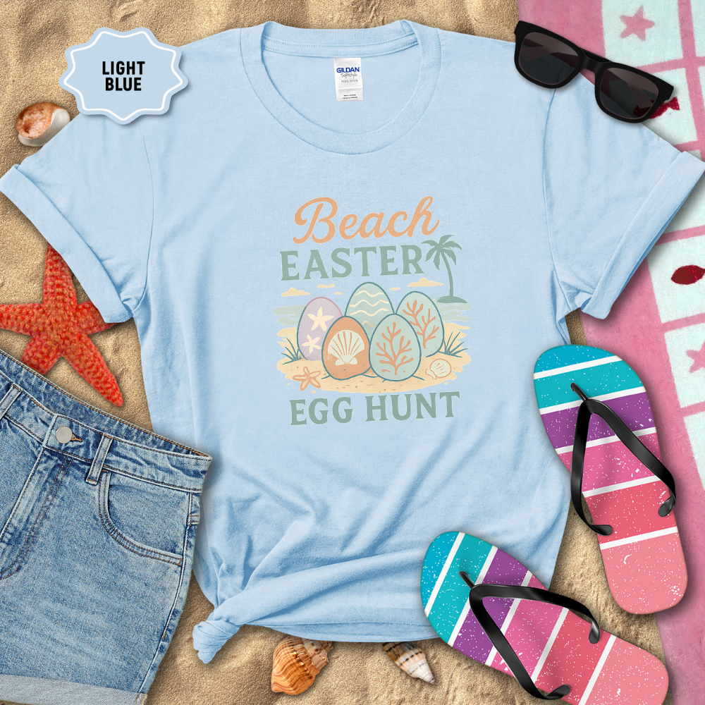 Light blue t-shirt with 'Beach Easter Egg Hunt' design on sand with beach accessories.