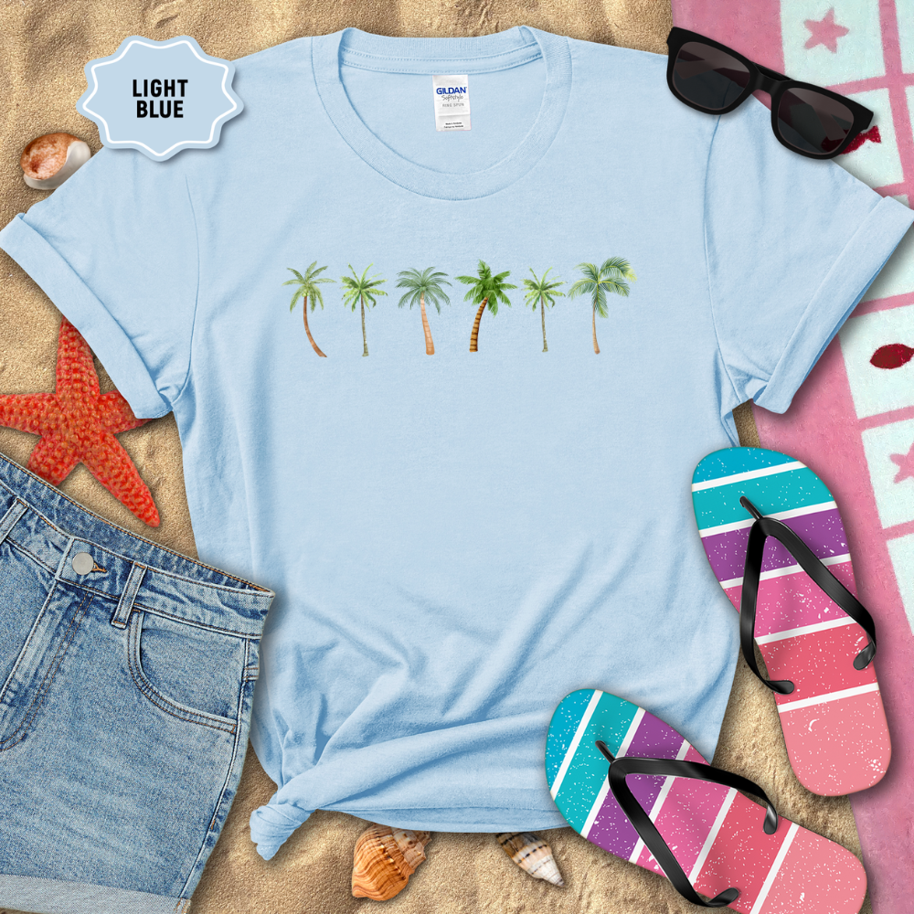 Light blue t-shirt with palm tree design on a sandy background with flip-flops and sunglasses.