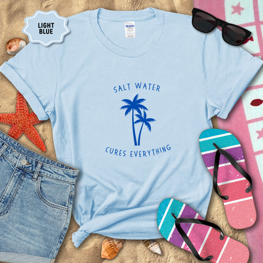 Light blue t-shirt with 'Salt Water Cures Everything' design on sand with beach accessories.