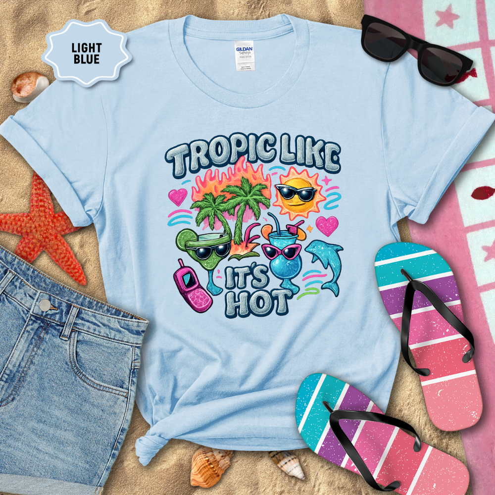 Light blue t-shirt with tropical-themed design on a sandy background with beach accessories.