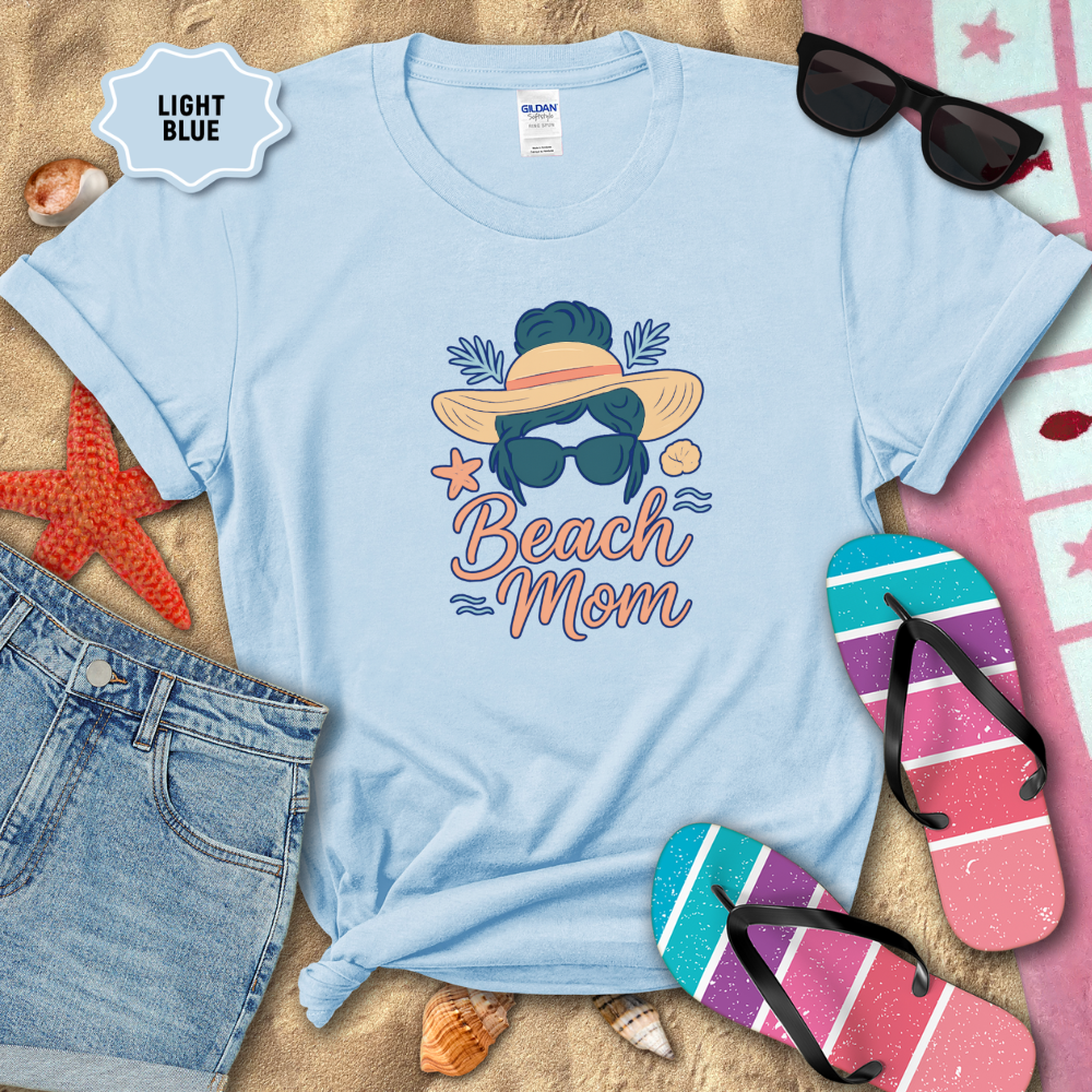 Light blue t-shirt with 'Beach Mom' design on sand with beach accessories.