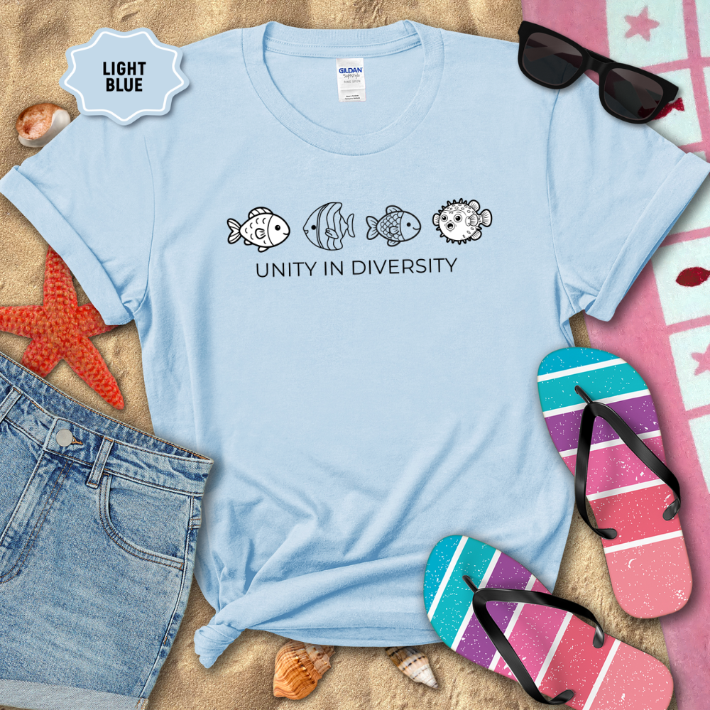 Light blue t-shirt with fish illustrations and 'Unity in Diversity' text on a sandy background with beach accessories.