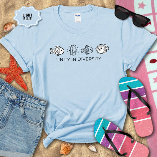 Light blue t-shirt with fish illustrations and 'Unity in Diversity' text on a sandy background with beach accessories.