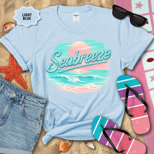 Light blue t-shirt with 'Seabreeze' design on a sandy background with beach accessories.