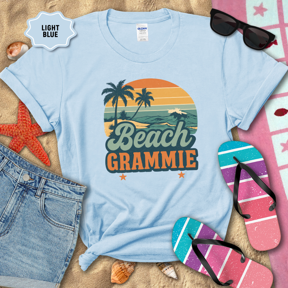 Light blue t-shirt with 'Beach Grammie' design on sand with beach-themed accessories.
