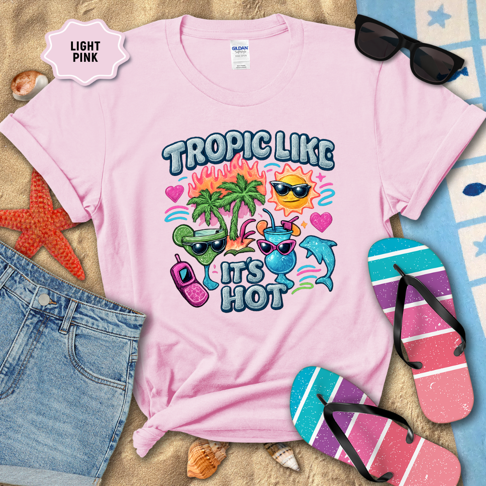 Light pink t-shirt with tropical-themed design on a sandy background with beach accessories.