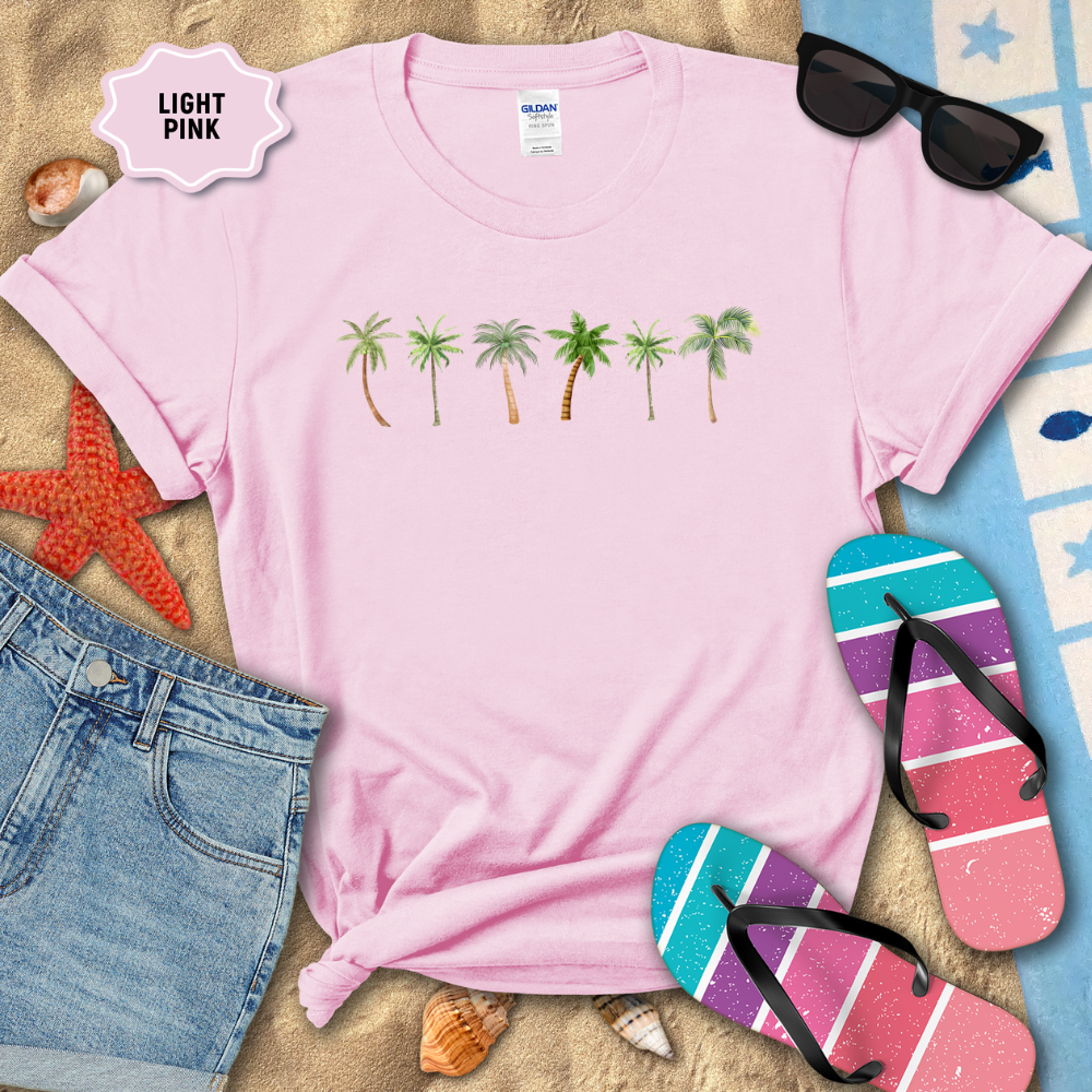 Light pink t-shirt with palm tree design on a sandy background with flip-flops and sunglasses.