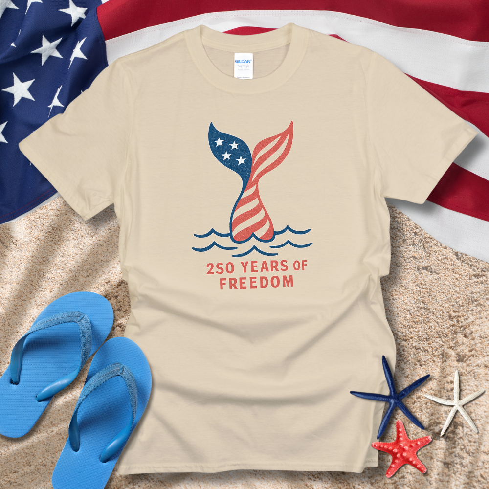 Beige t-shirt with '250 Years of Freedom' design on sand with American flag in background