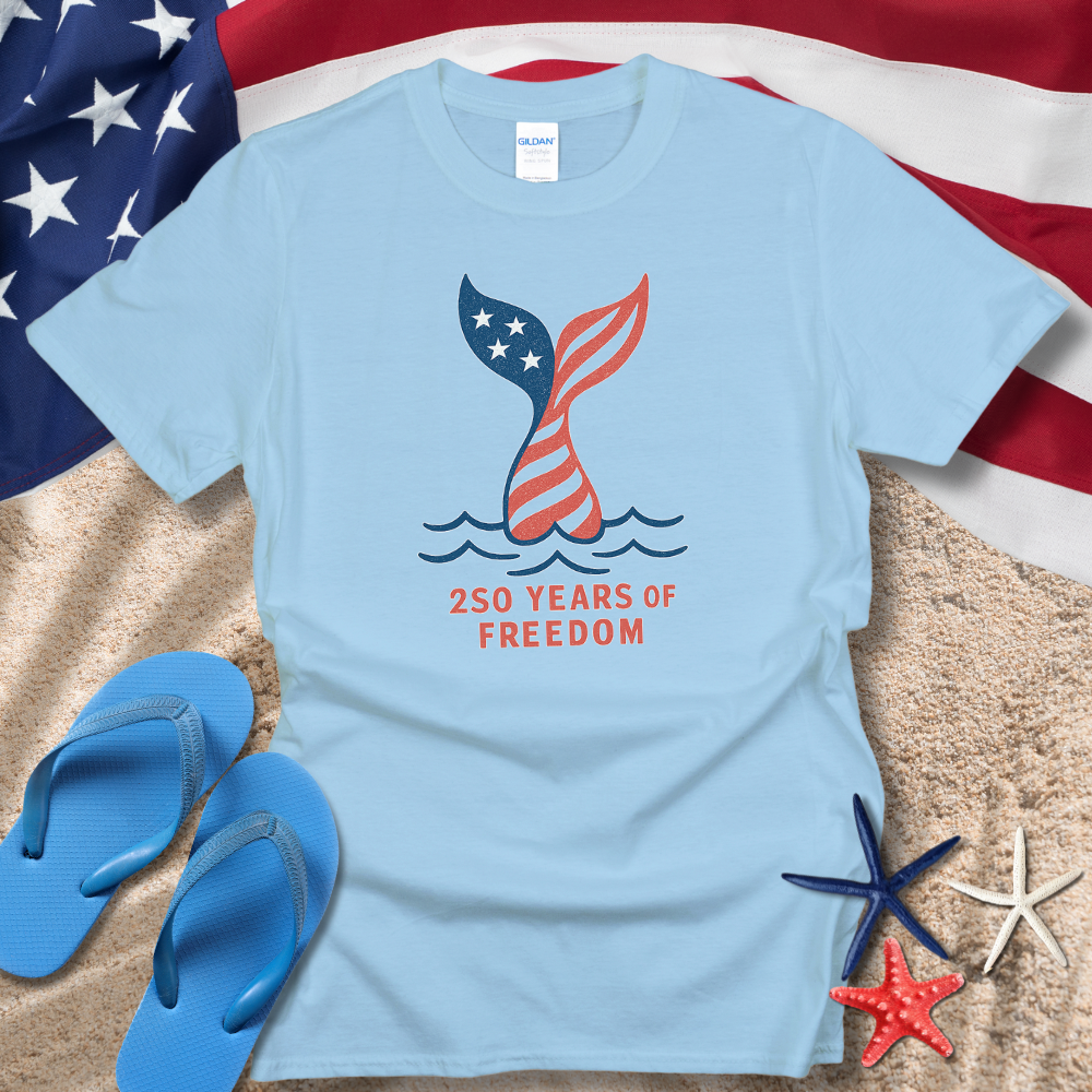 Light blue t-shirt with American flag design and '250 Years of Freedom' text on a beach setting with American flag, flip-flops, and starfish.