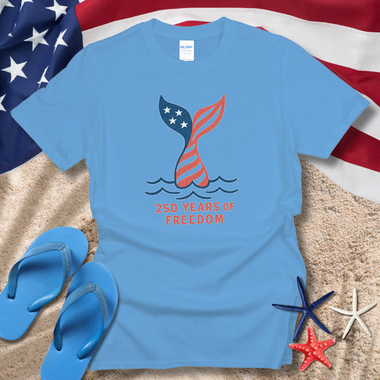 Blue t-shirt with American flag design and '250 Years of Freedom' text on sand with American flag in background