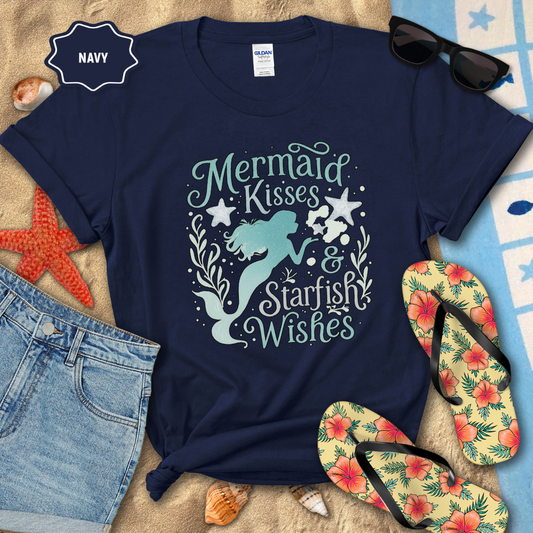 Navy t-shirt with mermaid design and text, surrounded by beach accessories on sand.