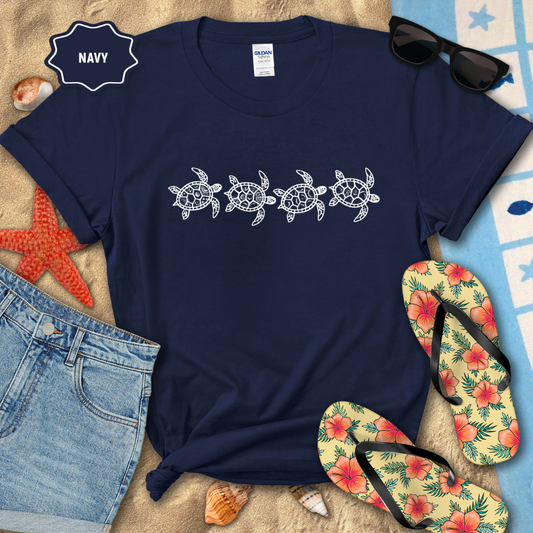 Navy t-shirt with turtle design on a beach setting with sunglasses, flip-flops, and denim shorts.