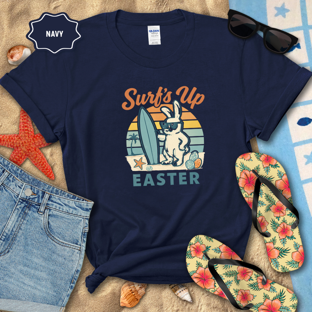 Navy t-shirt with 'Surf's Up Easter' design on a beach-themed background with sunglasses, flip-flops, and beach accessories.