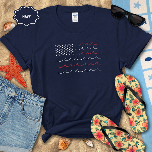 Navy t-shirt with American flag design on a beach setting with sunglasses, flip-flops, and denim shorts.