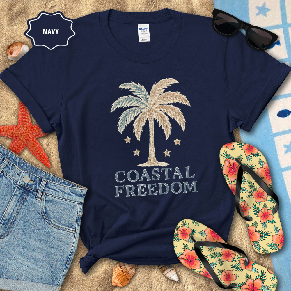 Navy t-shirt with palm tree design and 'Coastal Freedom' text, surrounded by beach accessories.