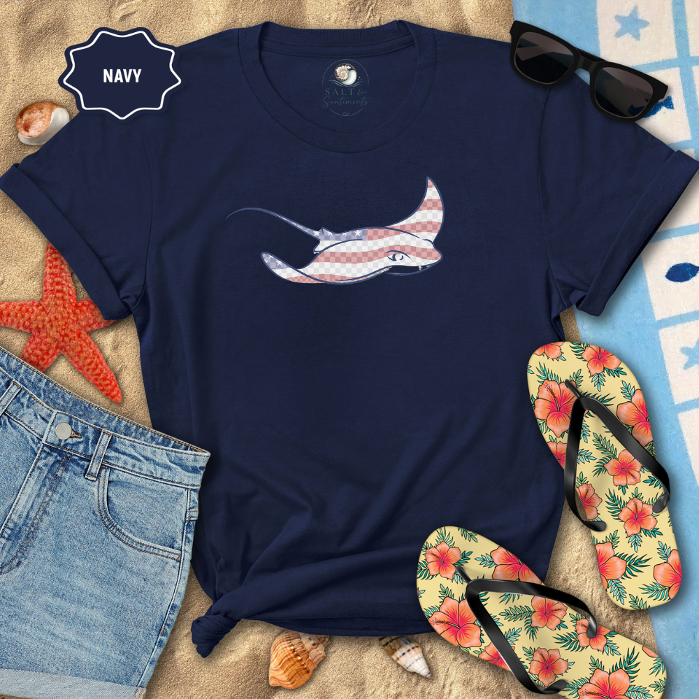 Navy t-shirt with a fish design on a beach setting with sunglasses, flip-flops, and denim shorts.