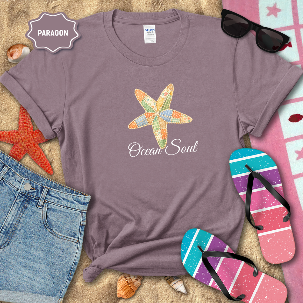 Purple t-shirt with starfish design and 'Ocean Soul' text, surrounded by beach-themed items on sand.