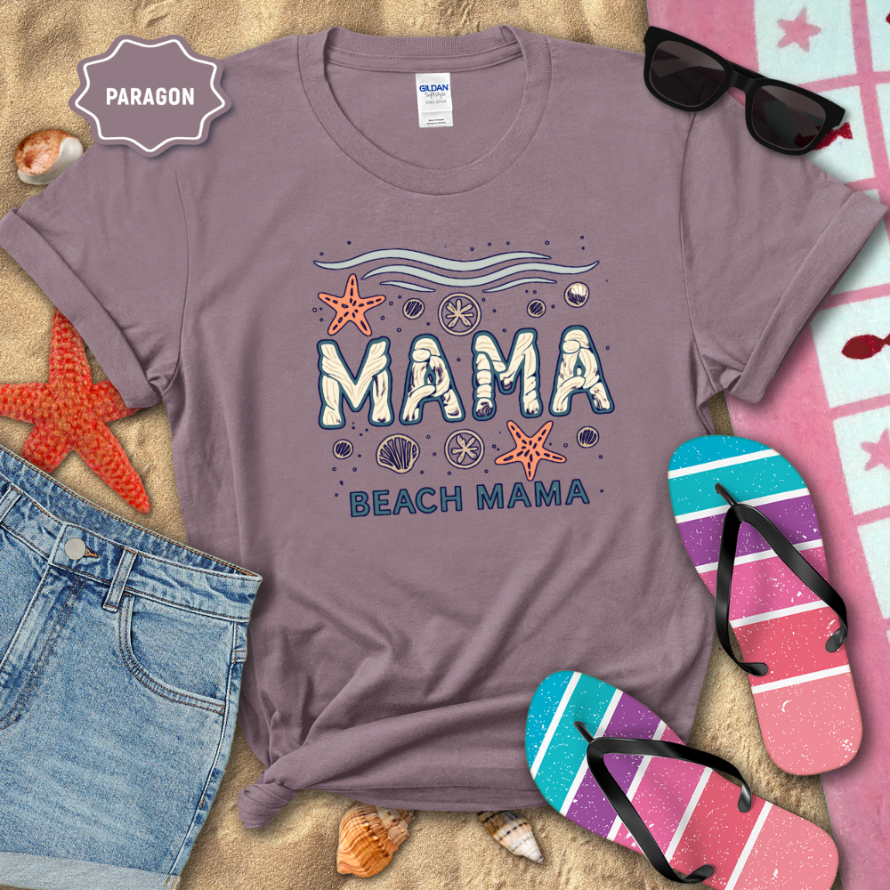 Purple t-shirt with 'Mama Beach Mama' design on a sandy background with beach accessories.