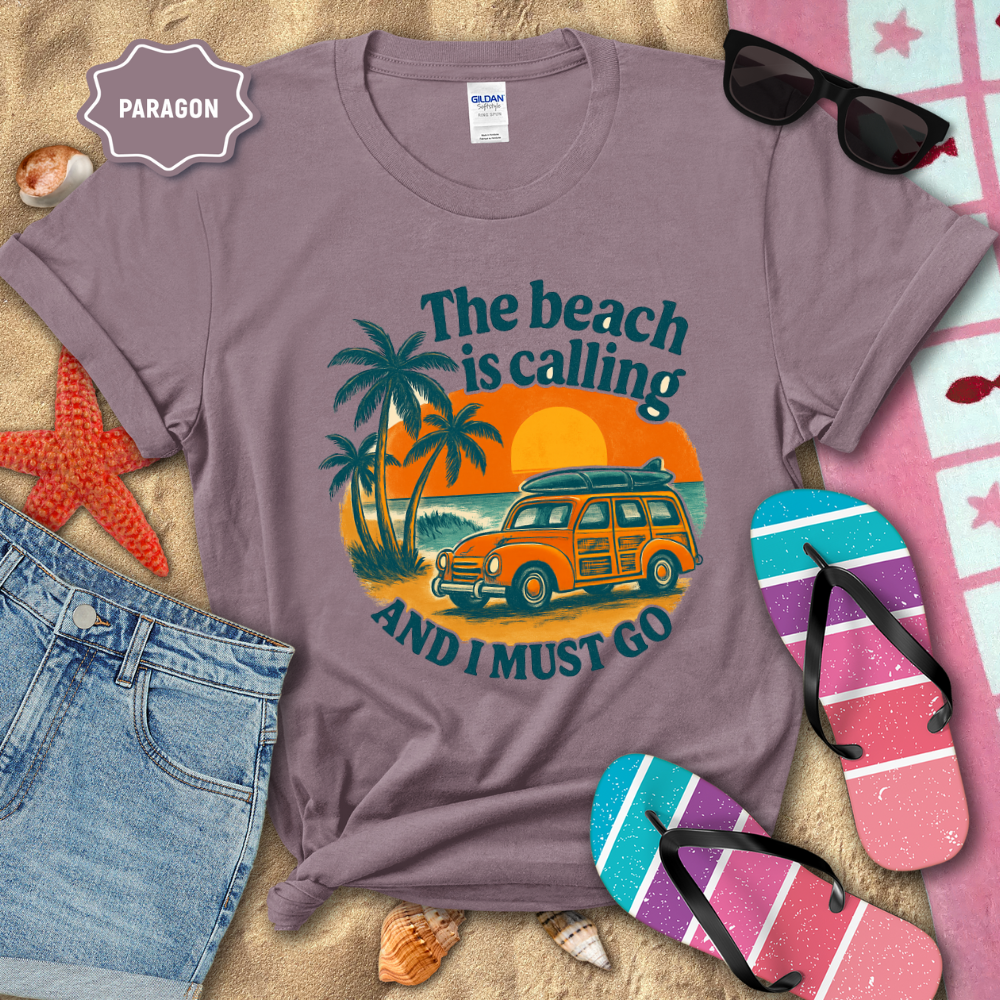 Purple t-shirt with beach-themed design featuring a van, palm trees, and text, surrounded by beach accessories.