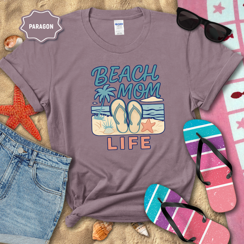 Purple t-shirt with 'Beach Mom Life' design on a sandy background with beach accessories.