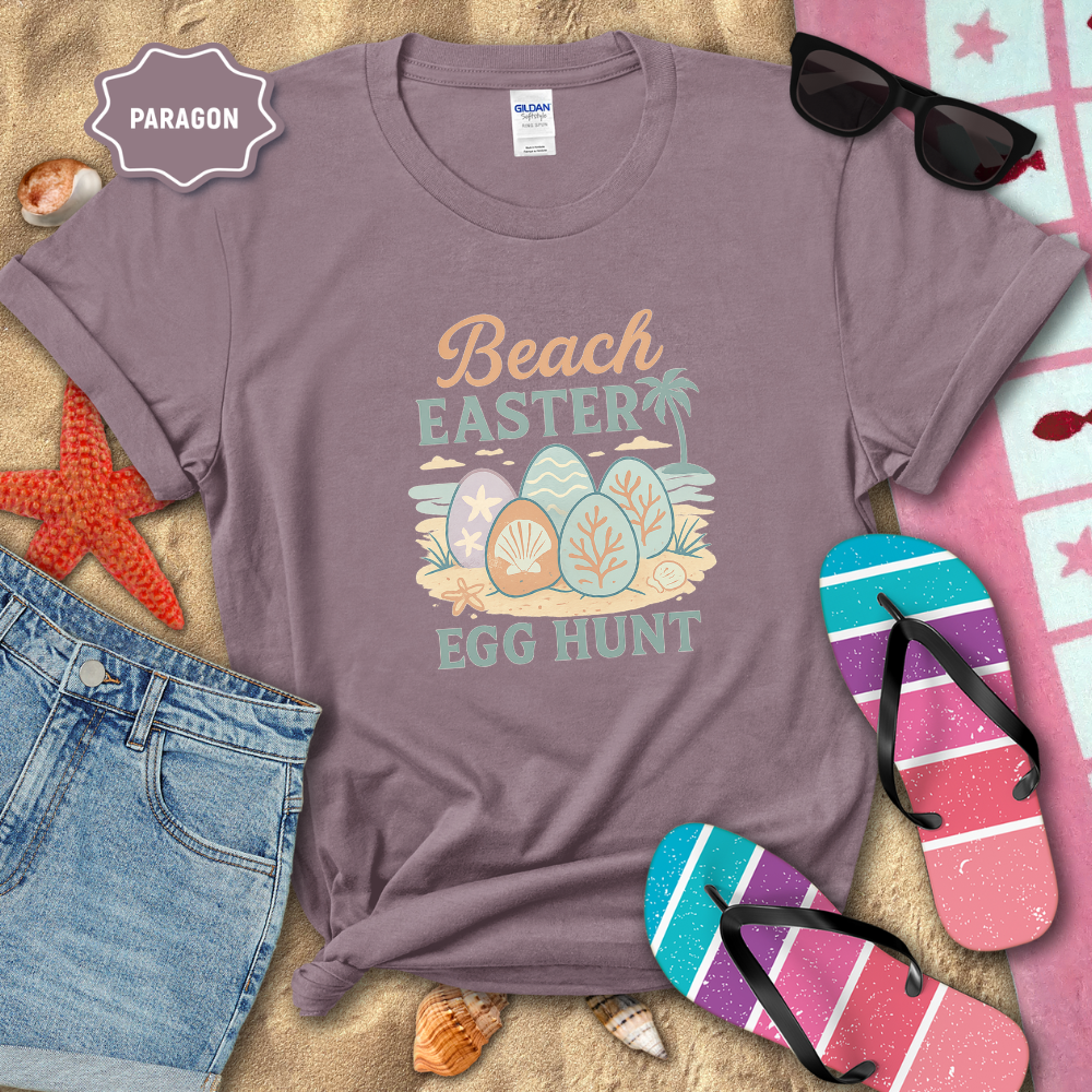 Purple t-shirt with 'Beach Easter Egg Hunt' design on a sandy background with flip-flops and sunglasses.