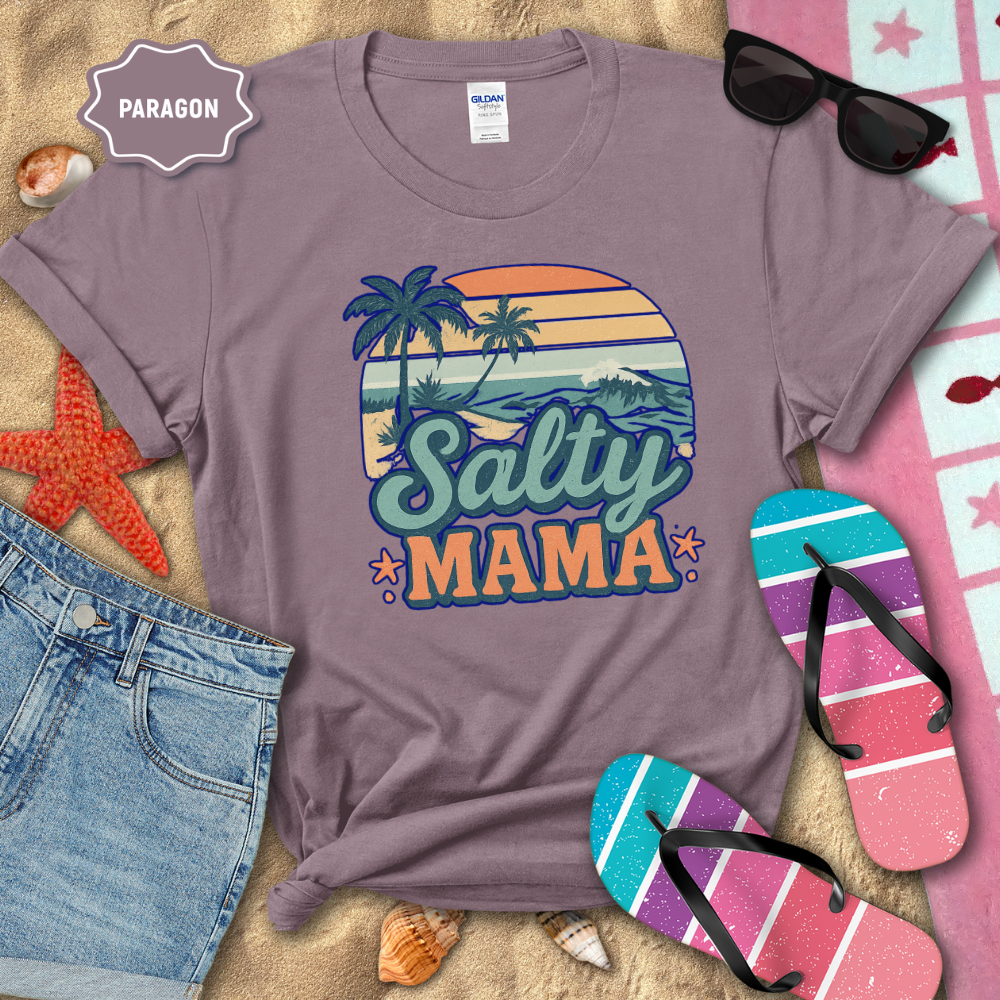 Purple t-shirt with 'Salty Mama' design on a beach-themed background with sunglasses, flip-flops, and denim shorts.