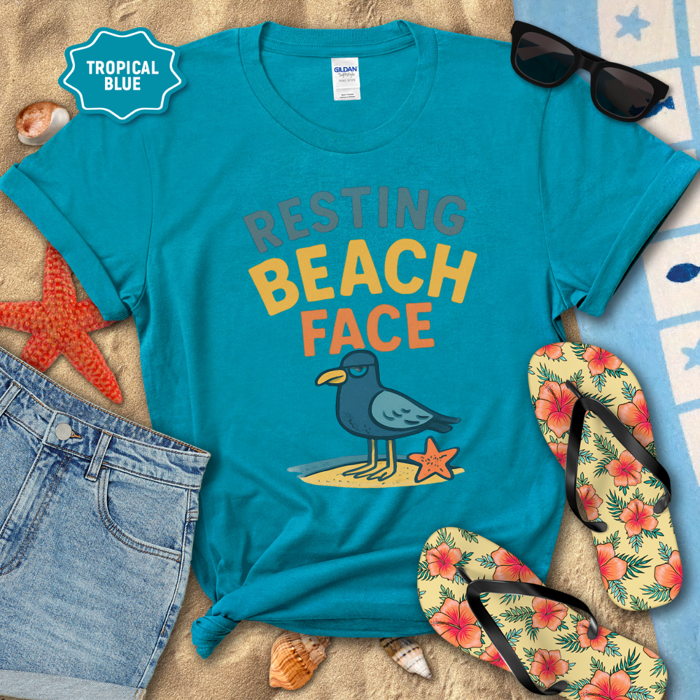 Blue t-shirt with 'Resting Beach Face' design on a sandy background with flip-flops and sunglasses.