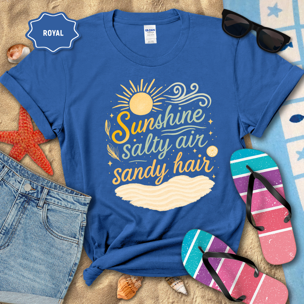 Blue t-shirt with 'Sunshine, Salty Air, Sandy Hair' design on a beach-themed background with sunglasses and flip-flops.