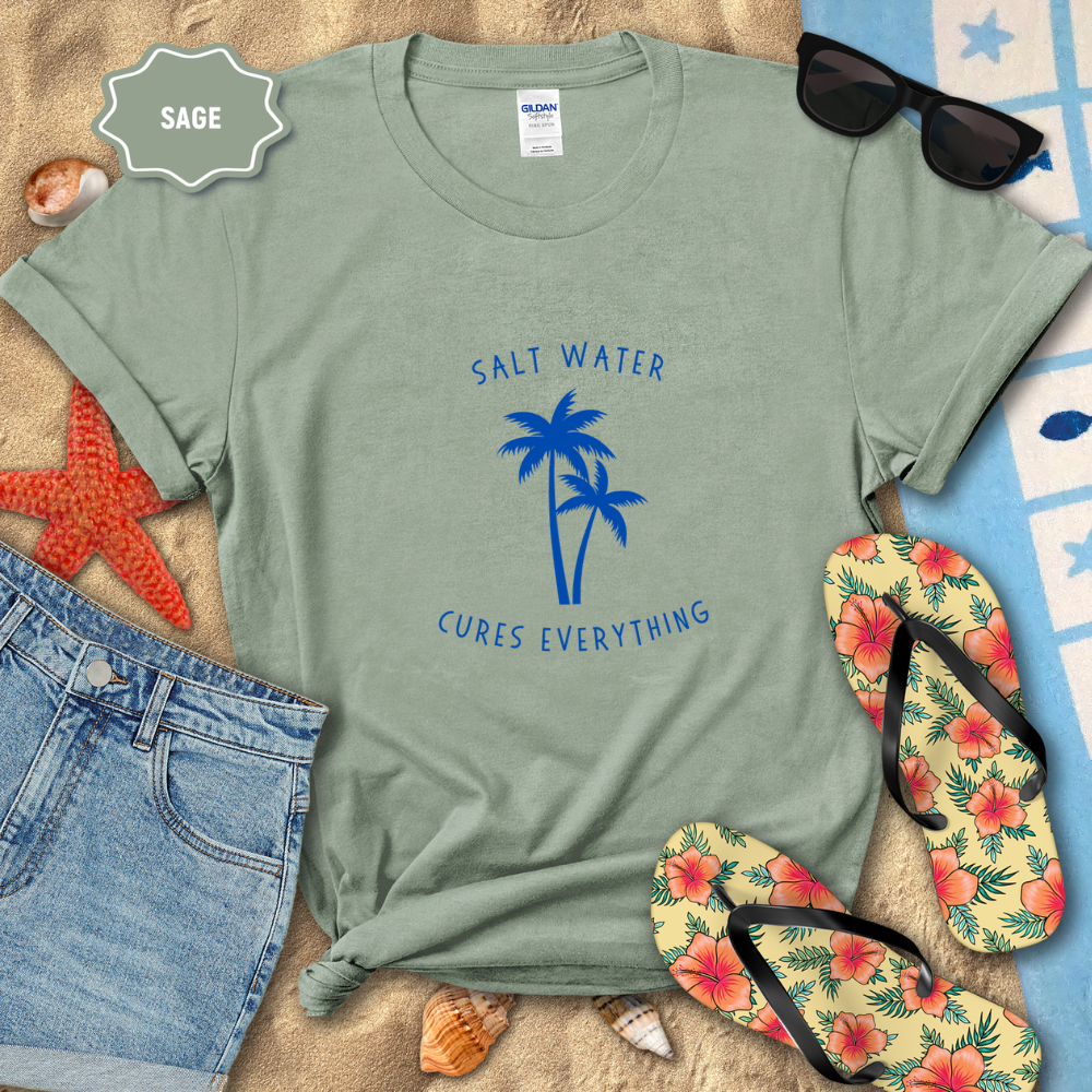 Sage green t-shirt with 'Salt Water Cures Everything' design on a beach-themed background with sunglasses, flip-flops, and starfish.